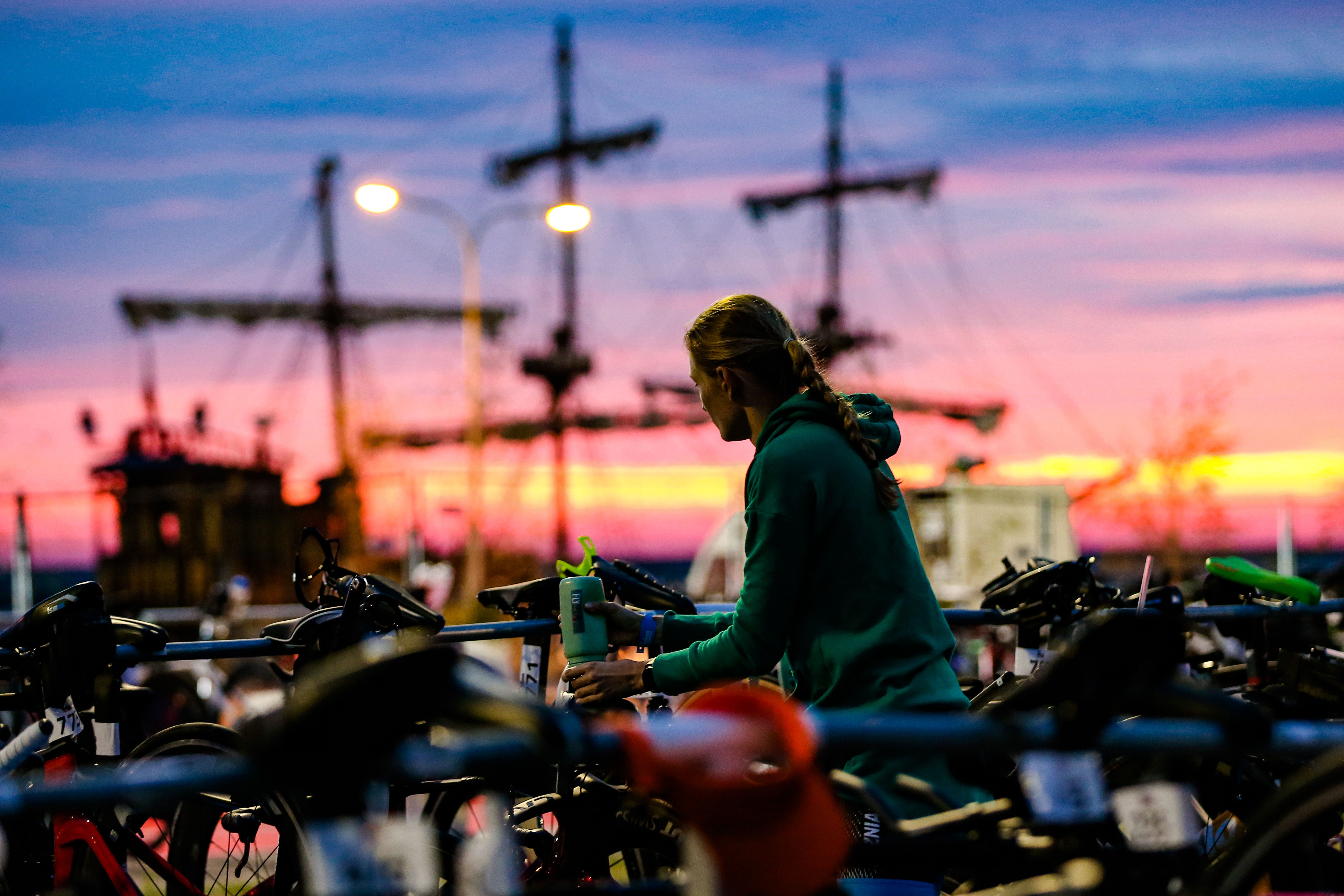 zawodniczka o wschodzie słońca z rowerem w strefie zmian - w tle żagle żaglowca