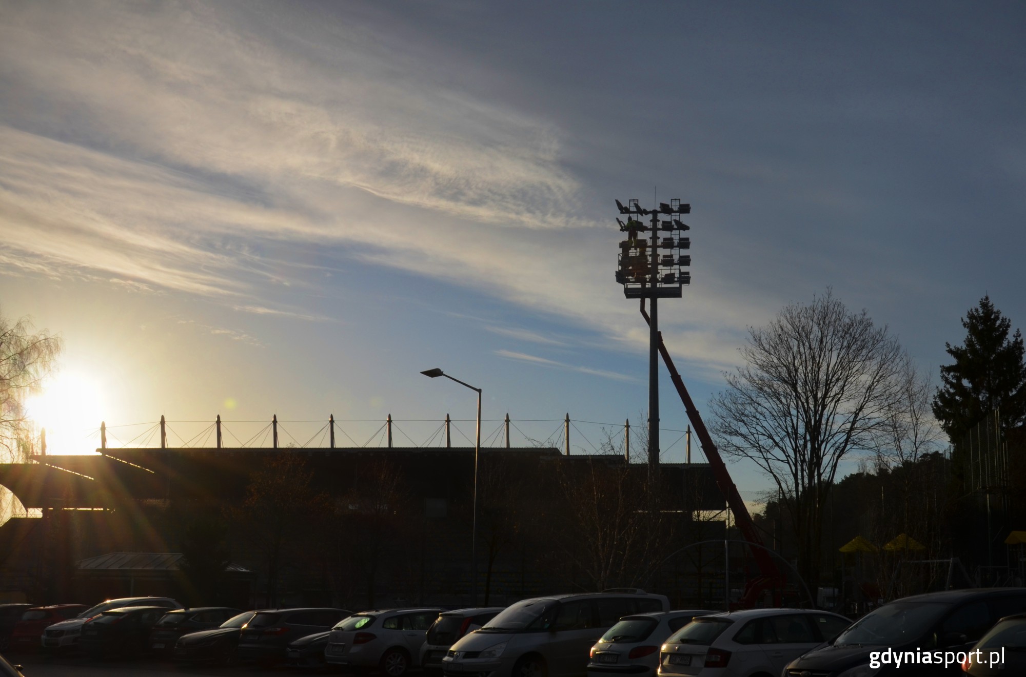 lampy w trakcie wymiany na tle przebijającego się słońca za stadionem