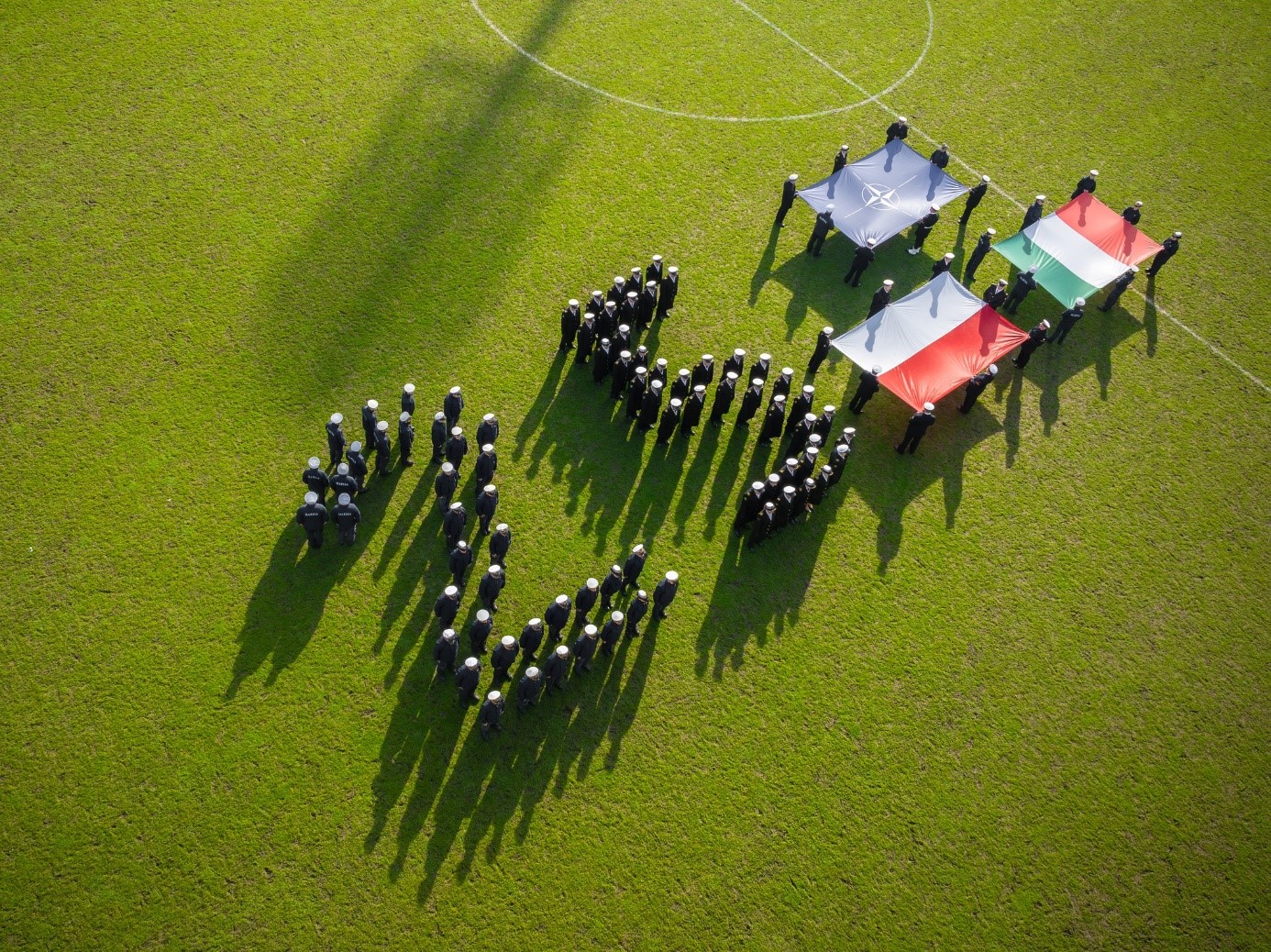 zdjęcie na Stadionie Miejskim przedstawiające żołnierzy ustawionych w liczbie 25 i flagi Polski, Włoch oraz NATO