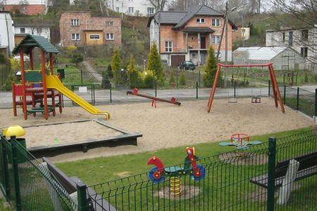 Plac zabaw przy ulicy Racławickiej: piaskownica, huśtawki, zjeżdżalnia i koniki.
