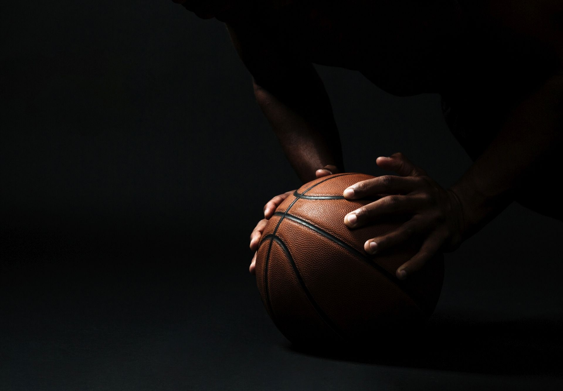 piłka do koszykówki w cieniu trzymana przez dłonie ciemnoskórej osoby 