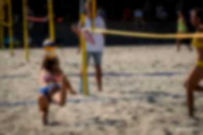 dziewczyna rzucająca się na piach w celu obrony piłki podczas meczu siatkówki plażowej. w tle siatka oraz sędzia
