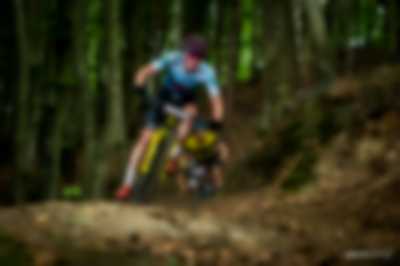 Kolarz MTB na żółtym rowerze w lesie ścigający się w zawodach. za nim kolejni 2 ścigający go zawodnicy