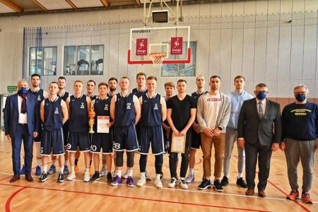 Reprezentacja koszykarzy AMW Gdynia stojąca na hali do wspólnego zdjęcia na tle kosza