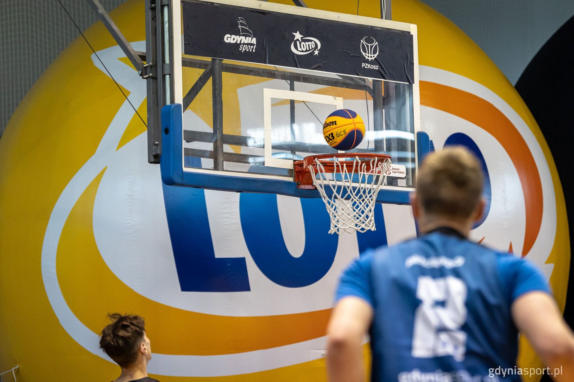 piłka na obręczy kosza na tle duży żółty balon sponsora