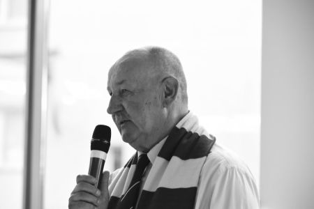 Janusz Kupcewicz z mikrofonem w ręce i szalikiem Arki na szyi