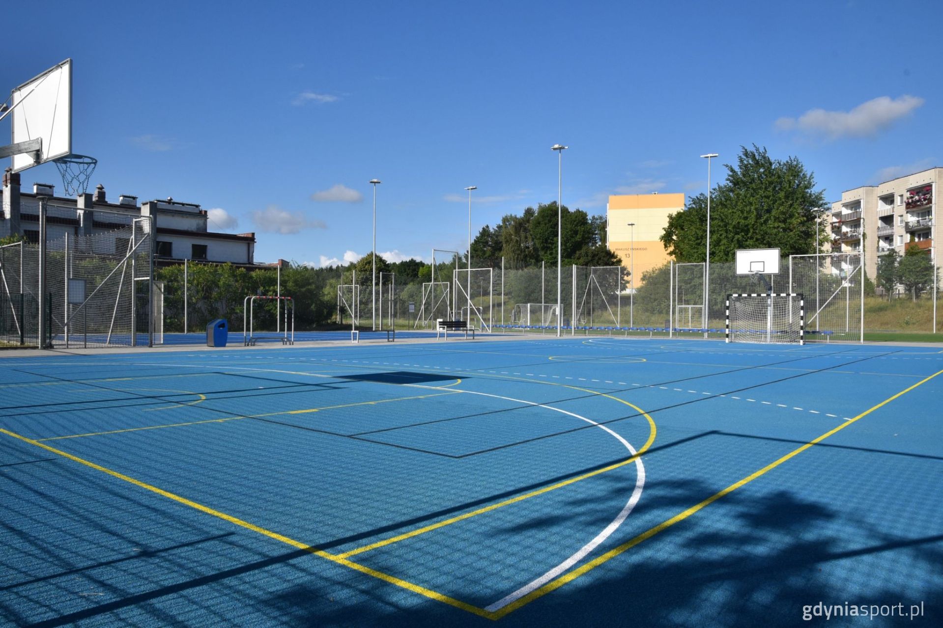 boisko trawiaste zdjęcie z rogu, w tle bloki i niebieskie niebo z chmurami