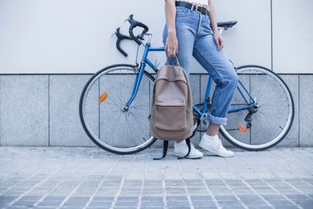 dolna sekcja kobiety z plecakiem w ręku na tle roweru partego o ścianę budynku